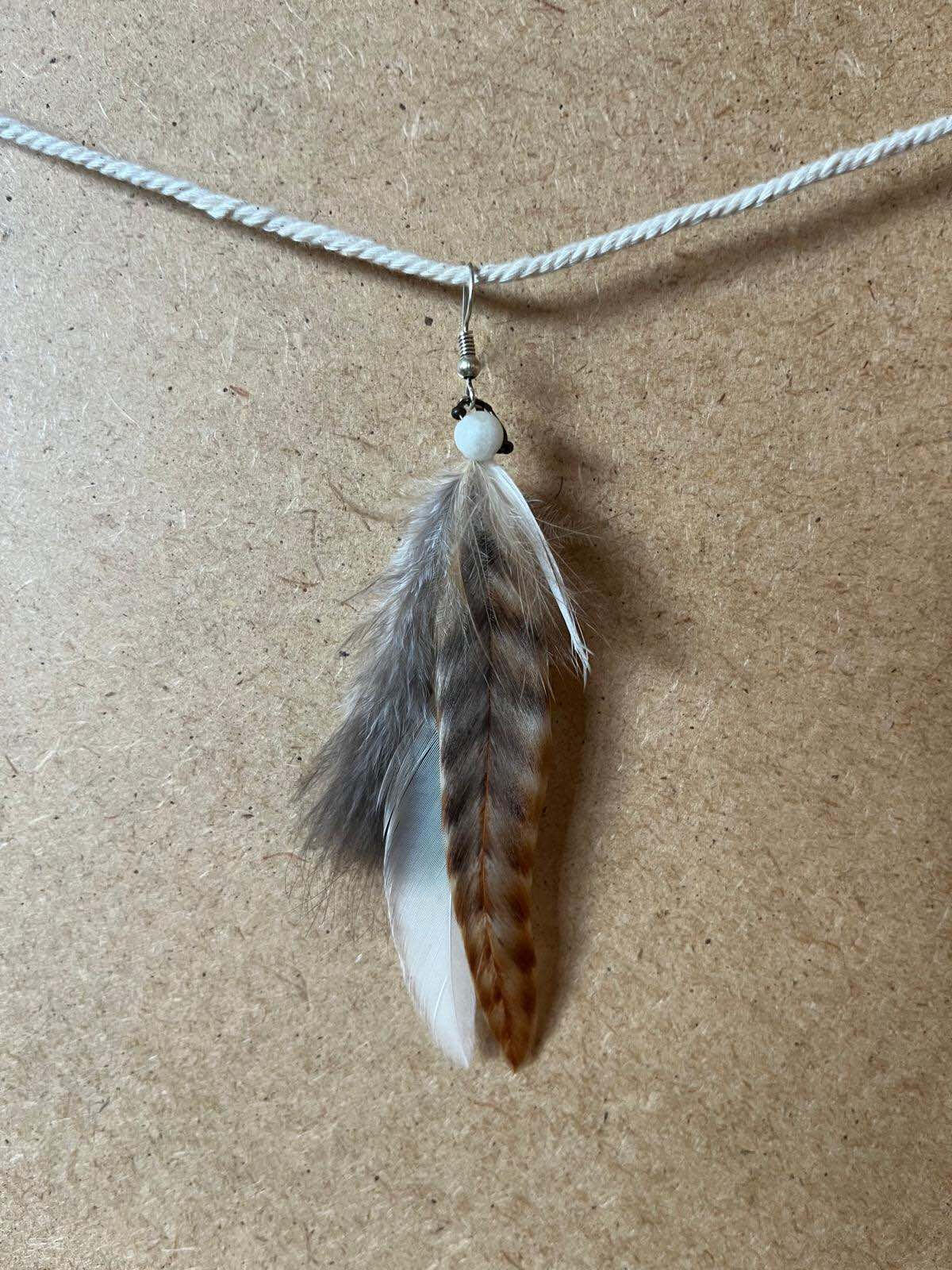 Pendiente artesanal Raíz Serena con plumas en tonos grises, blancos y marrones de inspiración natural