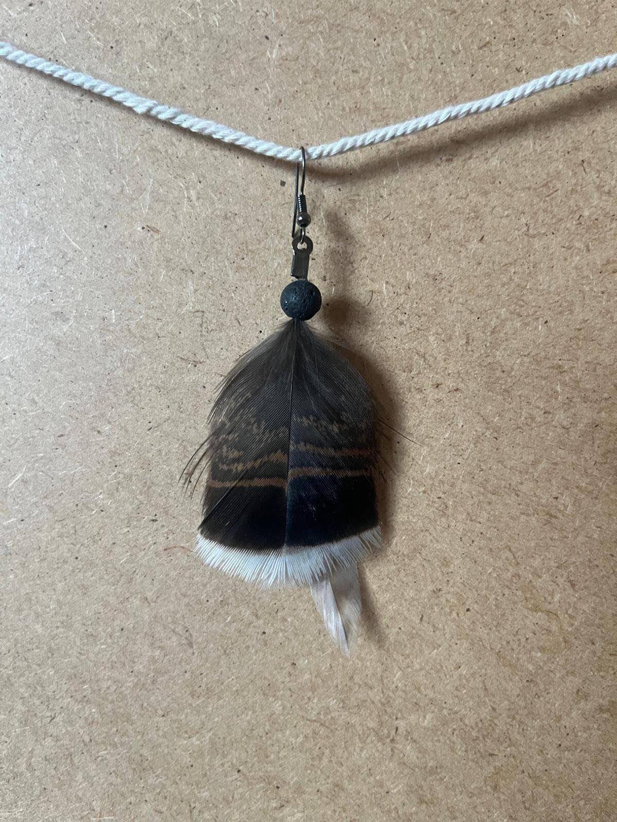 Pendiente artesanal Noche Raíz con pluma oscura y base clara en composición sobria y natural