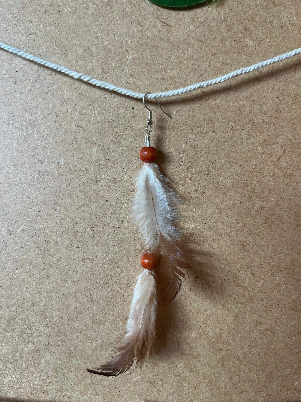 Pendiente artesanal Semilla de Calma con plumas claras y cuentas en tono cálido de caída delicada